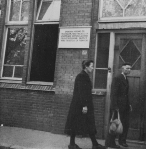 876761 Afbeelding van twee mensen die het gebouw Oudegracht 33 (Piusschool) dat o.a. in gebruik is als opvang voor ...